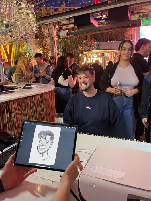 Rían drawing a laughing guest live on an iPad at a busy bar event