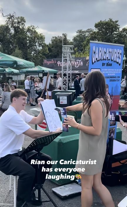Rían laughing as he shows a guest her paper caricature at Leopardstown Racecourse, captioned 'Rían our Caricaturist has everyone laughing'